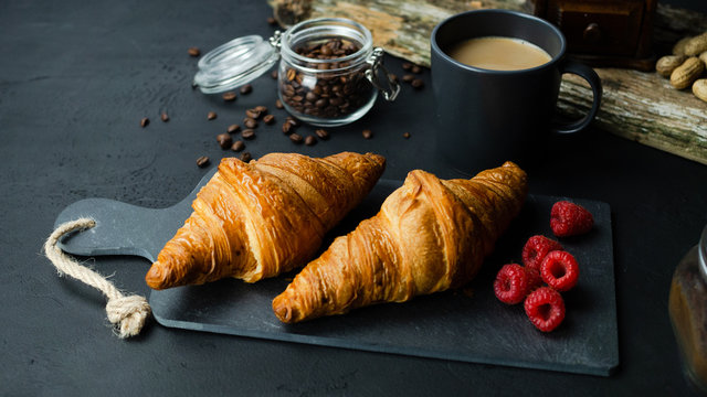 Croissant z malinami leżący na kamiennej desce. Ciemne tło, widok z g&oacute;ry.