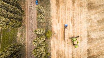 A beautiful new combine harvester dumps grain into a truck trailer on the field. Aerial view