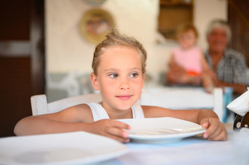 Cute little girl at the table in a cafe waiting for dinner