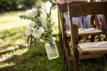 Hanging Flowers Next to a Wooden Folding Chair for an Outside Wedding Ceremony and a Wooden Fan on the Seat