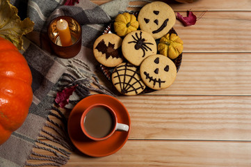 The Concept Of Halloween. A scarf, a Cup of coffee with milk, autumn leaves, a candle, delicious homemade cookies with spiders, bats, terrible emoticons, cobwebs on a wooden background.