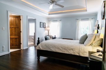 Fototapeta na wymiar Master bedroom with king size bed and tray ceilings with uplighting and hradwood floors