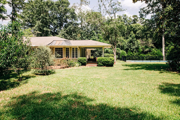 Back Rearview of exterior white cream brick 1950's house with black shutters and a large porch patio and also with a lawn lot with curb appeal