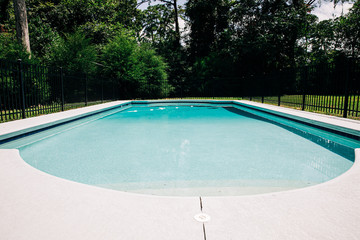 view of backyard swimming pool outside of a home with a large lot. There is a black metal fence in front of  the pool for child safety.