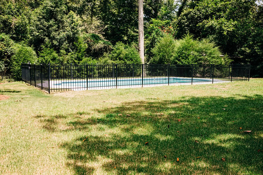 view of backyard swimming pool outside of a home with a large lot. There is a black metal fence in front of  the pool for child safety.