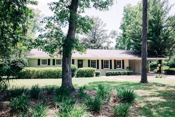 Front view of exterior white cream brick 1950's house with black shutters