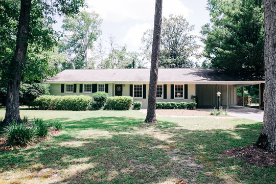 Front view of exterior white cream brick 1950's house with black shutters