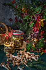 seasonal mushroom picking. Preparations for the winter, making homemade marinades. Marinated mushrooms in a glass jar standing on a wooden table with mushrooms. Forest in autumn.