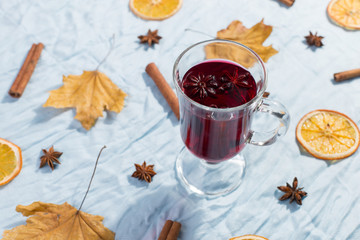 A cup of mulled wine with spices, dry leaves and oranges on the table. Autumn mood, a method to keep warm in the cold, copy space, morning light.
