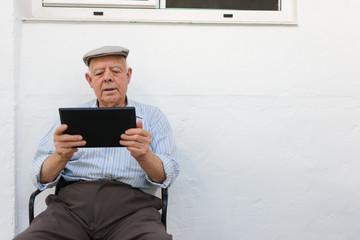 Elderly man is using a tablet in the yard of his house