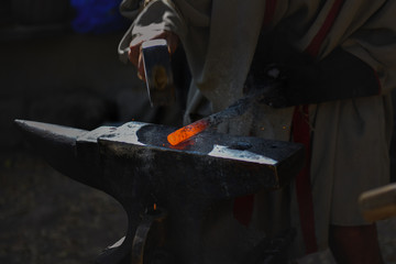 A blacksmith beats a hammer on red-hot metal on an anvil.