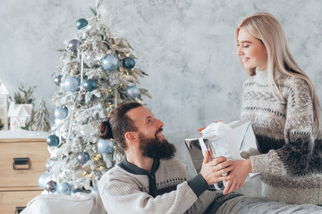 Romantic winter holidays. Lady giving present to her boyfriend. Couple happy to celebrate Christmas at home.