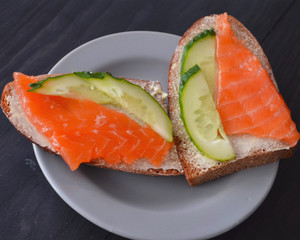Healthy breakfast. sandwich with salmon and cucumber, brown bread and butter on a wooden background.