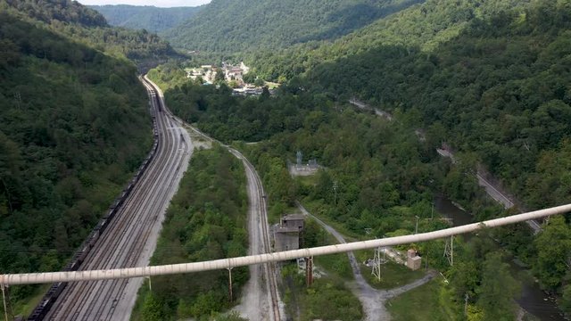 Aerial pull back showing railroad tracks in valley and abandoned coaling tower and newer coal slurry pipeline in Whitesville, West Virginia.