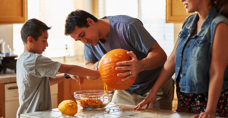 hispanic american family carving pumpkin into jack o lantern at home