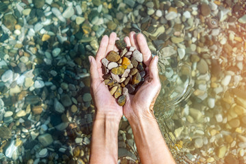 Women's hands with a handful of sea stones under water, holds in the clear sea water. Top view