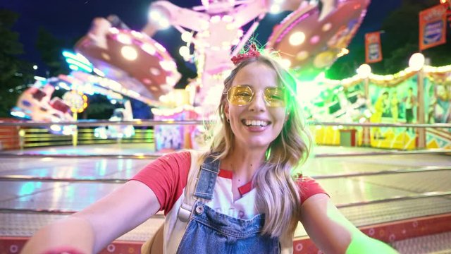 Charming happy young blonde woman grimacing and having fun while taking selfie photo at amusement park