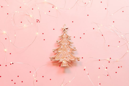 Christmas greeting card. Top view of golden fir tree ornament and LED string lights on star pattern pink background. Copy space. - Powered by Adobe