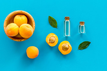 Apricot kernel oil among apricots and leaves on blue background top view pattern