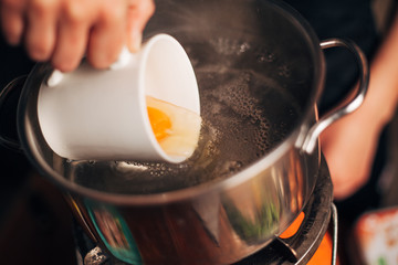 Chef pouring egg in a boiling water