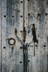 Old wooden door with doorknob. Chain and padlock framed in a hole