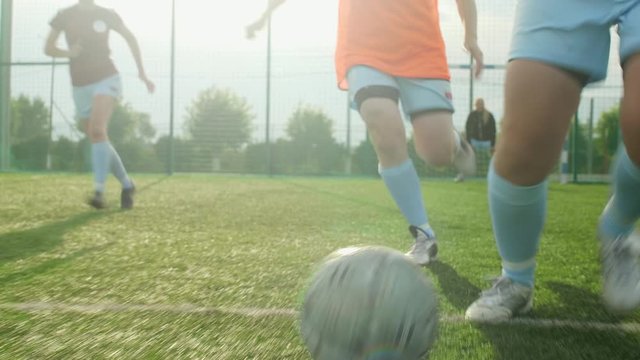 Low section shot of female soccer forward dribbling ball during match on outdoor playground in summer