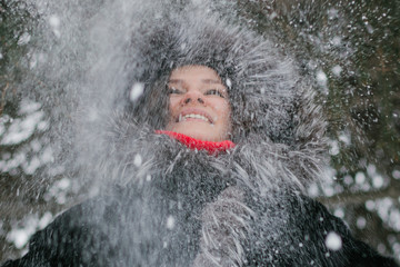 Girl in a fluffy fur hat lifted her head up smiling. Before her flying snow flakes.