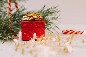 Christmas composition. Fir tree branch, red gift box, candy canes with gold confetti on white  background.