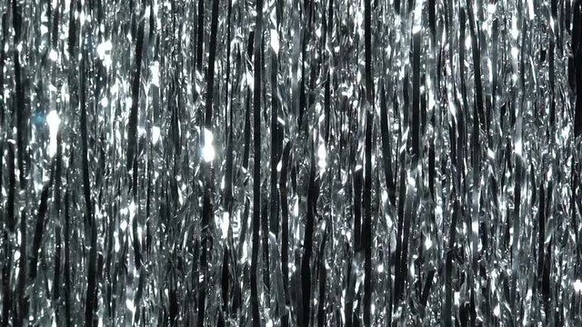 Silver rain from tinsel. Dynamic background in shining lights and sparkling particles. Beautiful silver background with shiny silver glitter sparkles. Festive mood. Christmas or holiday theme