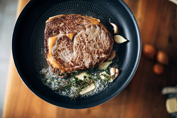 Overhead shot of  ribeye being prepared in a skillet with butter, thyme and garlic