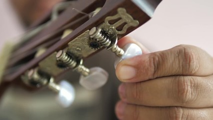 Close-up hands of man spinning tuner knob of acoustic classic guitar for fine tuning to standard key , Music instrumental for jazz and easy listening music style select focus shallow depth of field