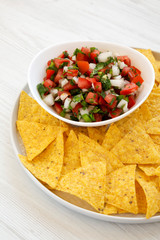 Pico de Gallo with gluten free tortilla chips on a white wooden surface, side view. Close-up.