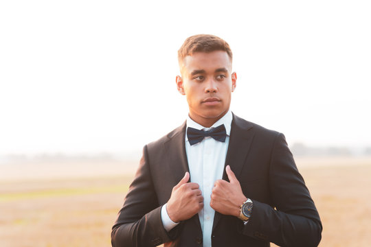A young handsome teen in black suit and bow tie with a confident and serious attitude look photographed in strong backlight