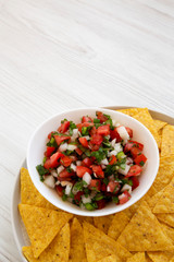 Pico de Gallo with gluten free tortilla chips on a white wooden table, side view. Copy space.
