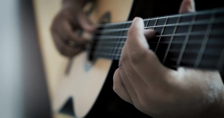 Slow-motion close-up hands of man playing acoustic classical guitar with dark and grain processed