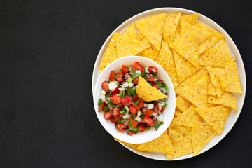 Pico de Gallo with gluten free tortilla chips on a black background, top view. Flat lay, overhead, from above. Space for text.