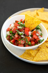 Pico de Gallo with gluten free tortilla chips on a black surface, side view. Close-up.