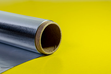Macro aluminum foil for baking and baking. Food foil roll, side view. Packaging foil on a yellow...
