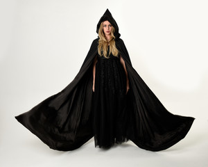 full length portrait of blonde girl wearing long black flowing cloak, standing pose  with  a white...