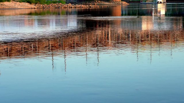 Reflections in water. Stunning riverbank shore with trains crossing a river bridge reflecting in the shiny surfacea at magical sunset. 