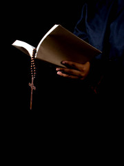 Portrait of hand holding a scripture with cross on dark background