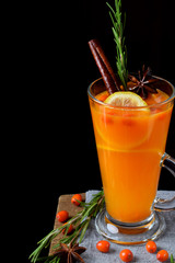 Fruit punch with sea buckthorn berries, citrus and spices in a tall glass on the edge of the table against black background