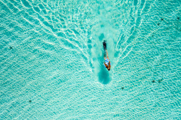 Top down view of a girl swimming in a lagoon. Aerial view of slim woman floating on the water....
