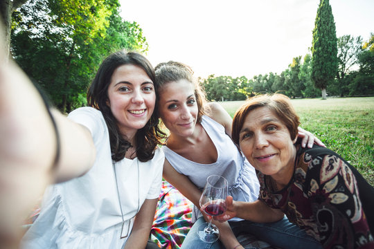 Mother and daughters take selfie embrace in a park at sunset on summer evening