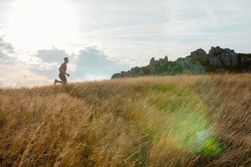 Trail running in the mountain fields. Young athletic man running and preparing for race.