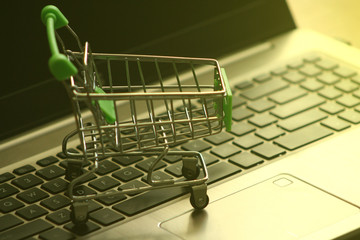 A mini dummy shopping trolley on a lapptop keyboard as a concept for online shopping, saving, business and making money as well as running a business.