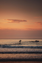 A man standing on a rock ready for surfing and waiting for the wave at colorful sunset light. Praia da Bordeira at the Algarve Coast in Portugal, Atlantic Ocean
