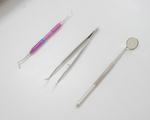 Fototapeta premium Dentist table with tools on a white background top view. A mirror, tweezers and a probe are on the doctors table. Oral hygiene, caries prevention, examination.