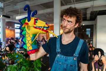Obraz premium Diverse group of people in yoga class. A portrait of a funny Caucasian guy as he looks towards a hand puppet with a peculiar and curious face. Motivational man stands at front of yogic workshop.