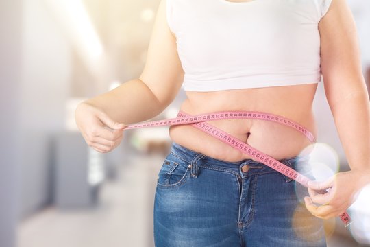 Overweight, fat woman measuring her stomach on background